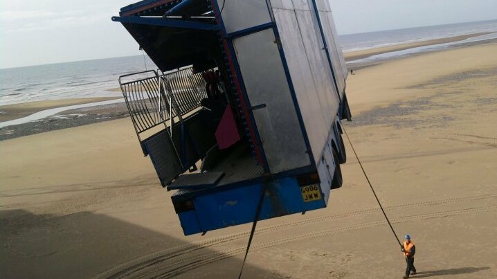 Freizeitpark-Anlage wird am Strand in Blackpool mit einem Kran bewegt, Mitarbeiter sichert den Transport