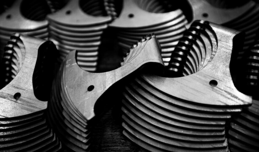 Das Schwarz-Weiß-Bild zeigt eine Nahaufnahme gestapelter Metallbauteile mit feinen Frässtrukturen und Bohrungen. Die hochpräzisen Kanten und symmetrischen Formen stehen für die exakte Fertigung im Prototypenbau von weba Deutschland. Dieses Bild unterstreicht die Qualität und Präzision, die für komplexe Bauteile in der Automobilindustrie erforderlich sind.