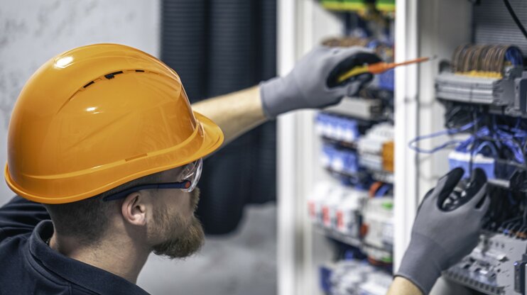 Elektromechaniker mit Schutzhelm prüft elektrische Steuerung und Verkabelung in einem Schaltschrank