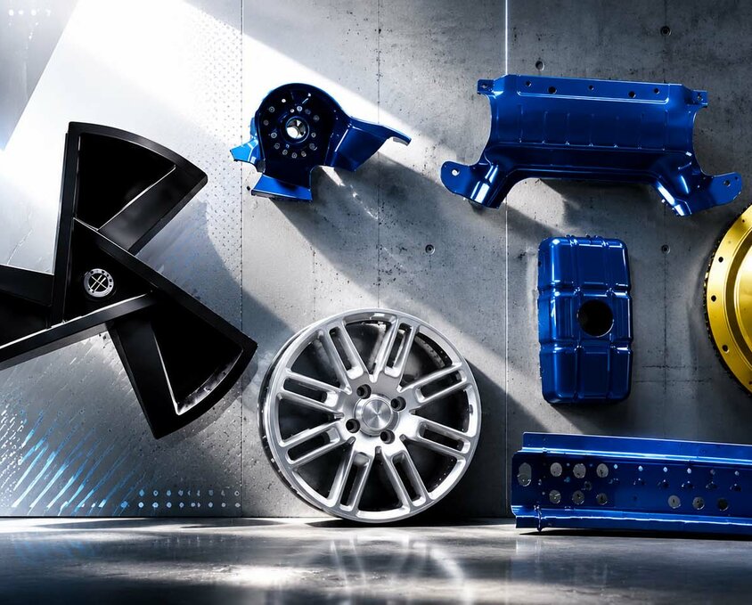 Das Bild zeigt eine Auswahl an Prototypenbauteilen von weba Deutschland. Zu sehen sind verschiedene komplex geformte Metall- und Kunststoffteile, darunter eine Lüfterflügelstruktur, ein Rad, sowie diverse verstärkte Komponenten in Blau, Schwarz und Gold. Diese hochwertigen Bauteile stehen für die Präzision und Innovationskraft von weba Deutschland im Bereich Prototypenbau und Umformtechnik für die Automobilindustrie.