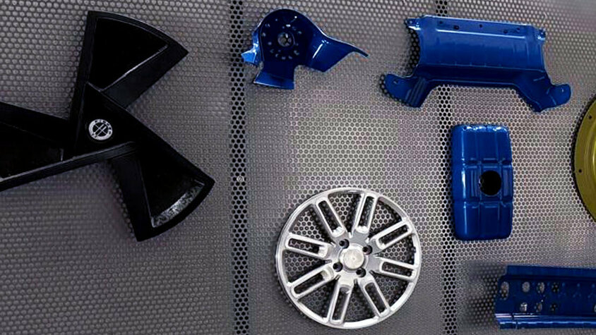 Das Bild zeigt eine Auswahl an Prototypenbauteilen von weba Deutschland. Zu sehen sind verschiedene komplex geformte Metall- und Kunststoffteile, darunter eine Lüfterflügelstruktur, ein Rad, sowie diverse verstärkte Komponenten in Blau, Schwarz und Gold. Diese hochwertigen Bauteile stehen für die Präzision und Innovationskraft von weba Deutschland im Bereich Prototypenbau und Umformtechnik für die Automobilindustrie.