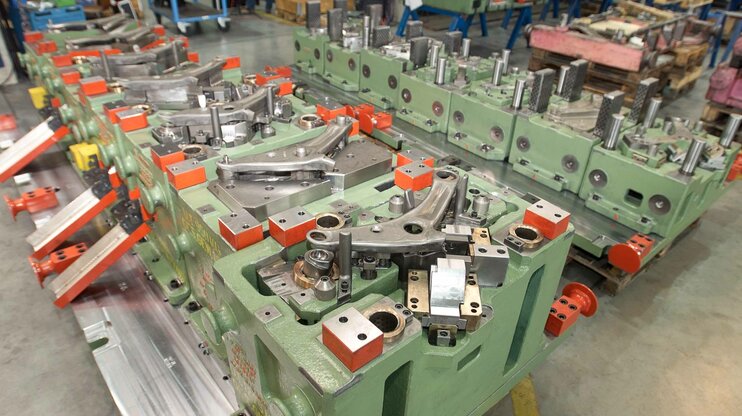 Transferwerkzeug für einen Querlenkerarm in der Automobilproduktion; komplexe Werkzeugaufspannung mit mehreren Formnestern und mechanischen Einheiten in der Werkhalle von weba Werkzeugbau.