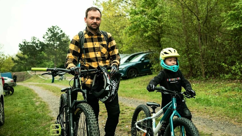 Radek Šimek steht mit Mountainbike und Helm neben seinem jungen Sohn, der mit Kinder-MTB und Helm startklar ist.