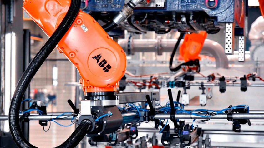 Series production & tool manufacturing at weba  An industrial robotic arm in tool manufacturing, working on a complex production line. The orange ABB robotic arm is equipped with various gripping and sensor tools and is used in series production and forming technology. In the background, additional mechanical components and wiring are visible, highlighting the state-of-the-art automation and precision in manufacturing technology.
