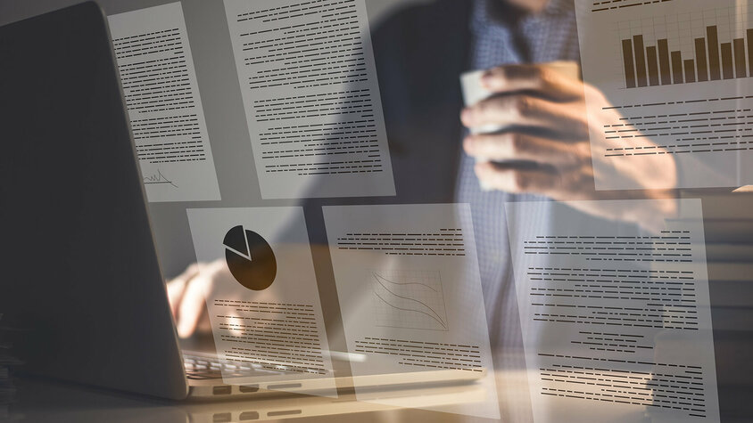 Ein Geschäftsmann sitzt vor einem offenen Laptop, während das Bild von digitalen Dokumenten überlagert wird, die Grafiken und Texte zeigen.