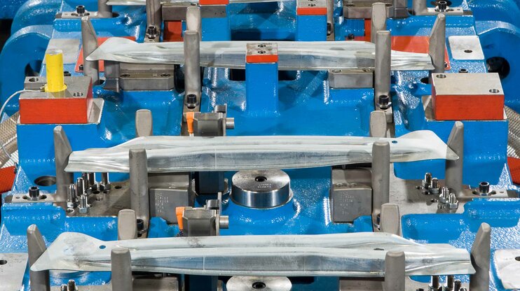 Transferwerkzeug zur Kaltumformung im Detail: Mehrere fixierte Blechteile in einem präzise gefertigten Werkzeug für die Herstellung von Türaufprallträgern in der Automobilindustrie.
