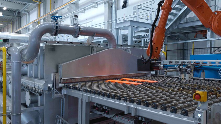 Automatisierte Warmumformungsanlage mit Roboterhandling und glühendem Stahlblech zur Herstellung hochfester Leichtbauteile.