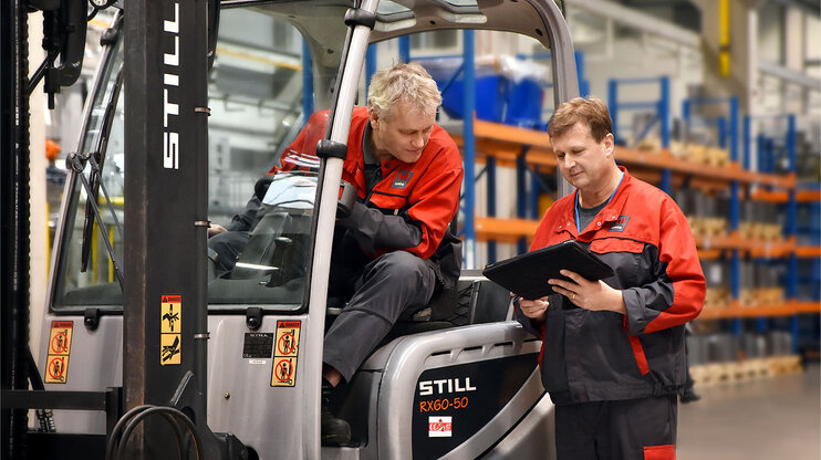 Dva pracovníci ve výrobě kontrolují pracovní dokumenty u vysokozdvižného vozíku ve skladovém prostoru