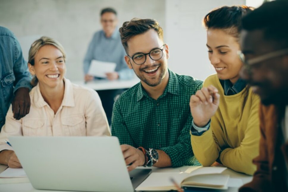 Fröhlicher Student hat Spaß beim Benutzen eines Laptops mit seinen Freunden im Klassenzimmer. Das Bild symbolisiert Praktikum Jobs in Steyr für Schüler und Studenten bei weba Werkzeugbau.