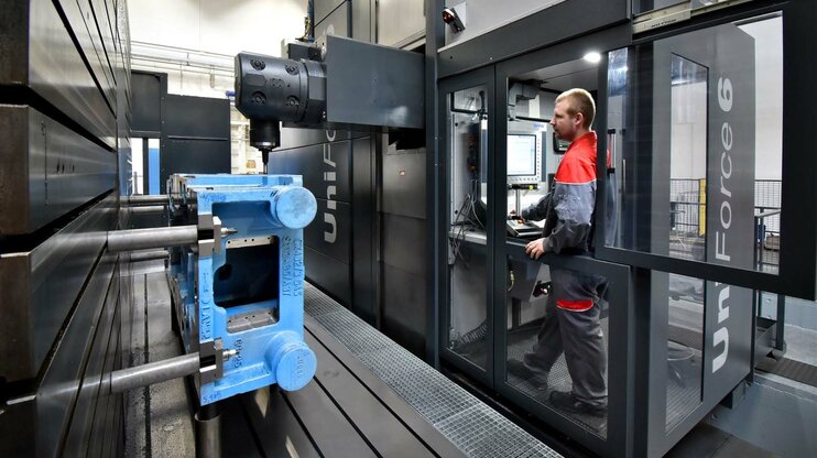 Ein Maschinenbediener steht im Bedienraum eines Bearbeitungszentrums der Marke SHW und beobachtet die Bearbeitung eines großen Gusses.