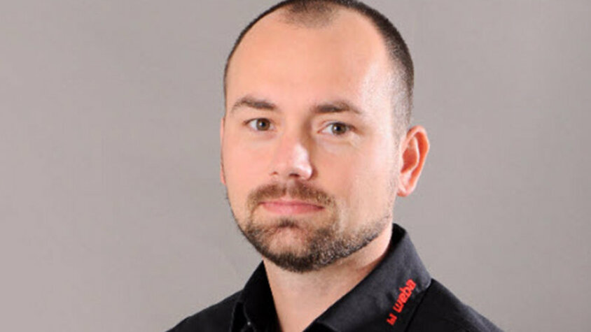 Porträt von Radek Šimek, Projektmanager bei weba Werkzeugbau, im schwarzen Firmenhemd vor neutralem Hintergrund.