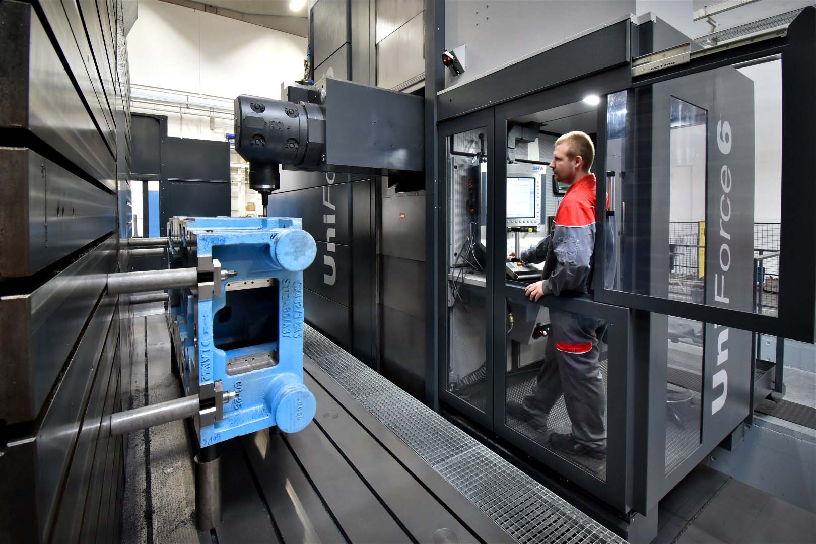 Ein Maschinenbediener steht im Bedienraum eines Bearbeitungszentrums der Marke SHW und beobachtet die Bearbeitung eines großen Gusses.