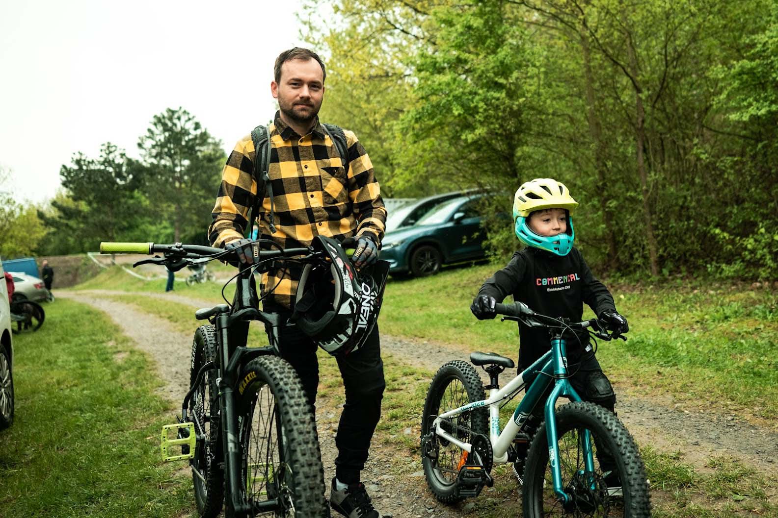 Radek Šimek steht mit Mountainbike und Helm neben seinem jungen Sohn, der mit Kinder-MTB und Helm startklar ist.