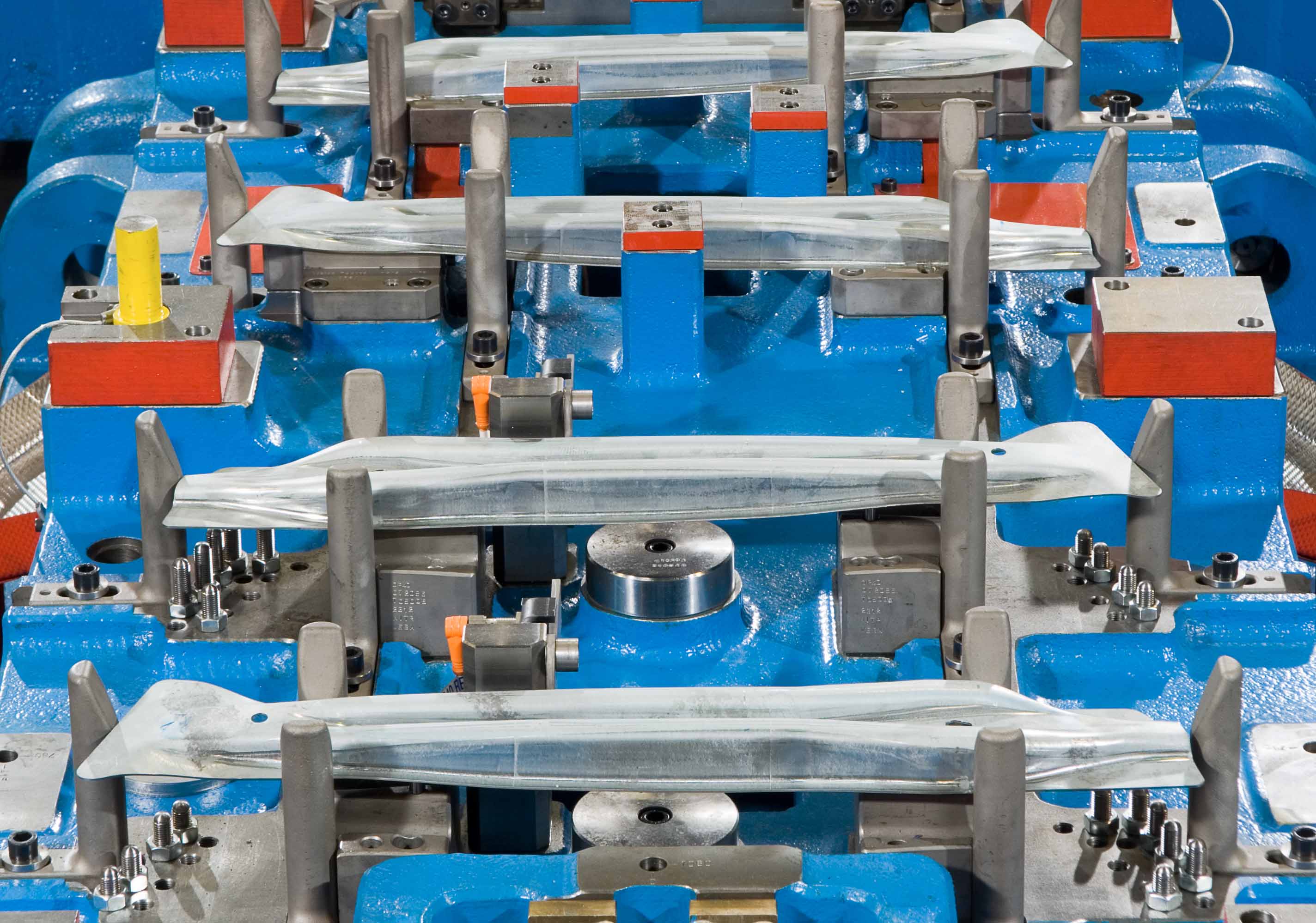 Transferwerkzeug zur Kaltumformung im Detail: Mehrere fixierte Blechteile in einem präzise gefertigten Werkzeug für die Herstellung von Türaufprallträgern in der Automobilindustrie.